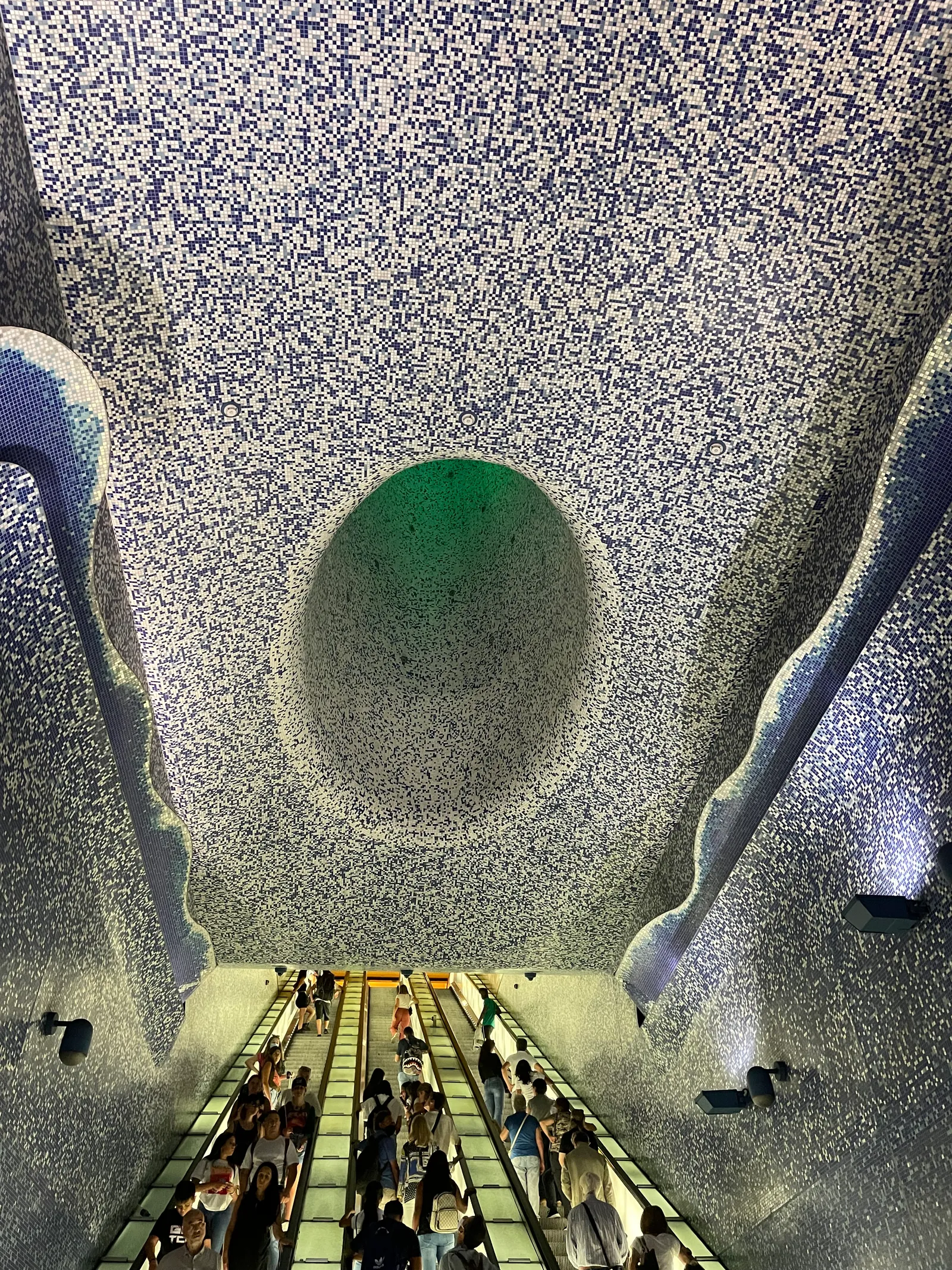 Looking down the escalator into Toledo metro station's deep, blue mosaic-covered oculus in Naples