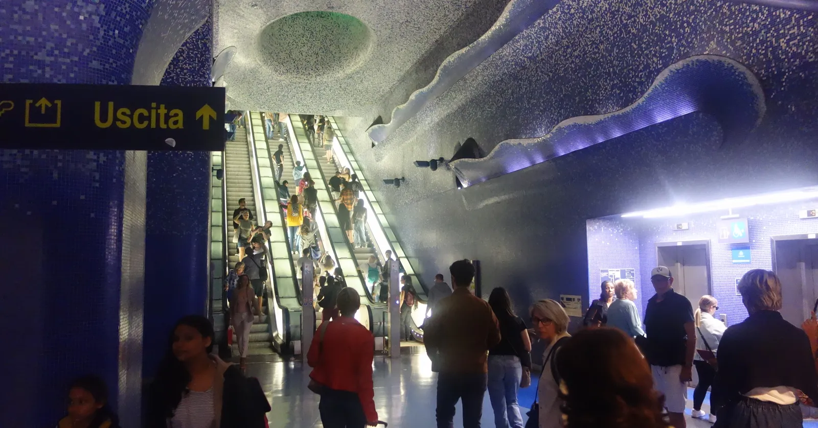 The mezzanine of Toledo metro station in Naples, escalators running down between walls and a vaulted ceiling covered in dark blue and white mosaic