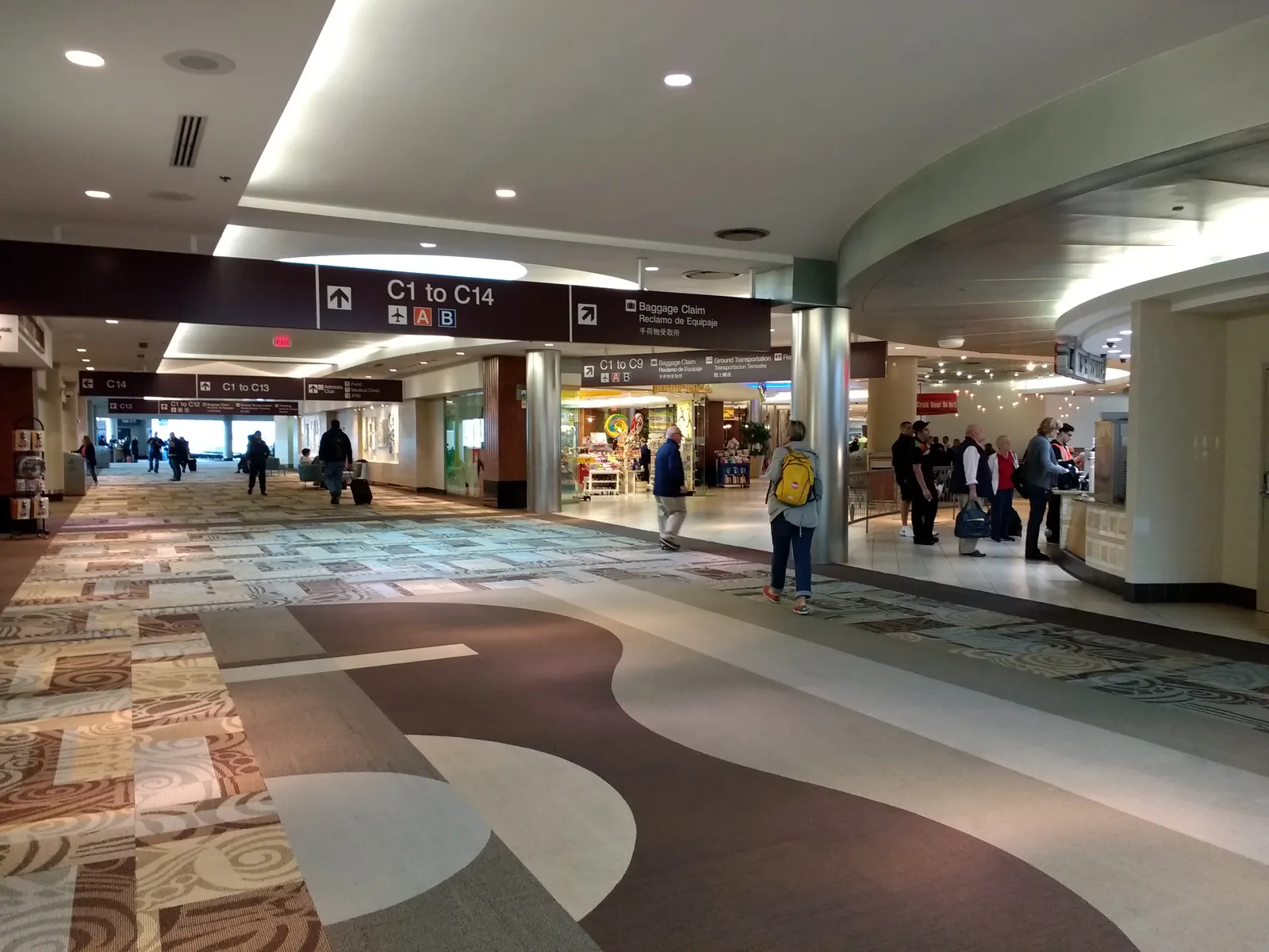 Concourse C at Nashville International Airport, with overhead signs reading C1 to C14, shops along the right side and passengers walking the patterned carpet