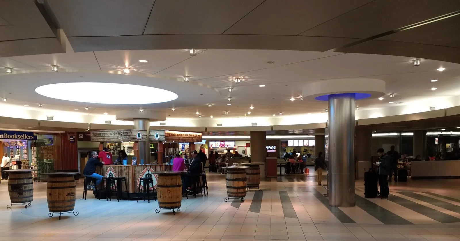 The marketplace inside Nashville International Airport's terminal, with whiskey-barrel tables and stools under a round skylight and shops around the edge
