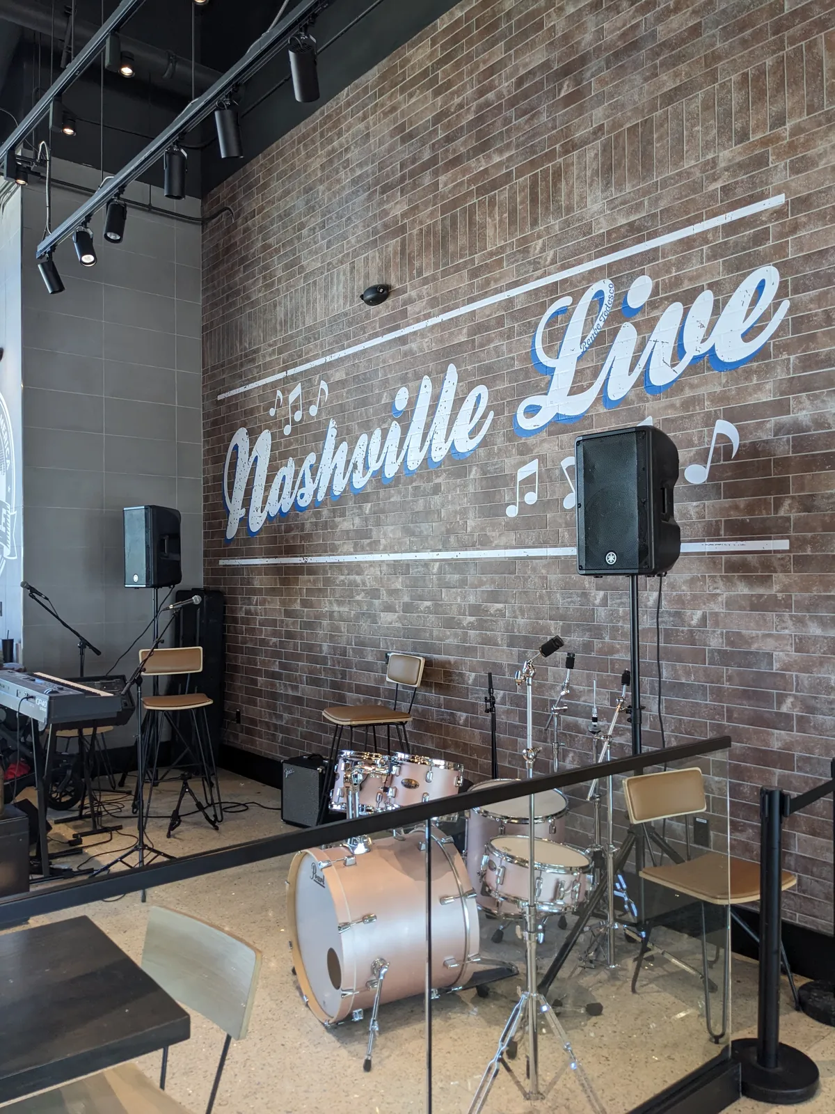 A live music stage inside Nashville International Airport, with a drum kit, keyboard and speakers set up against a brick wall painted with the words Nashville Live