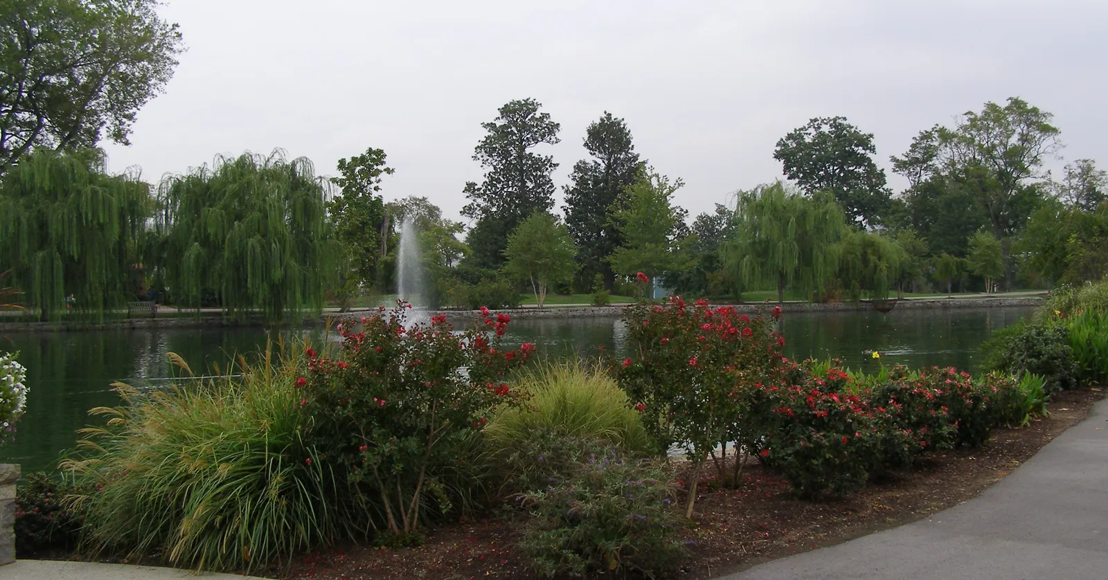 Lake Watauga in Centennial Park, Nashville, with a jet fountain in the middle, weeping willows along the far bank and flowering shrubs in the foreground