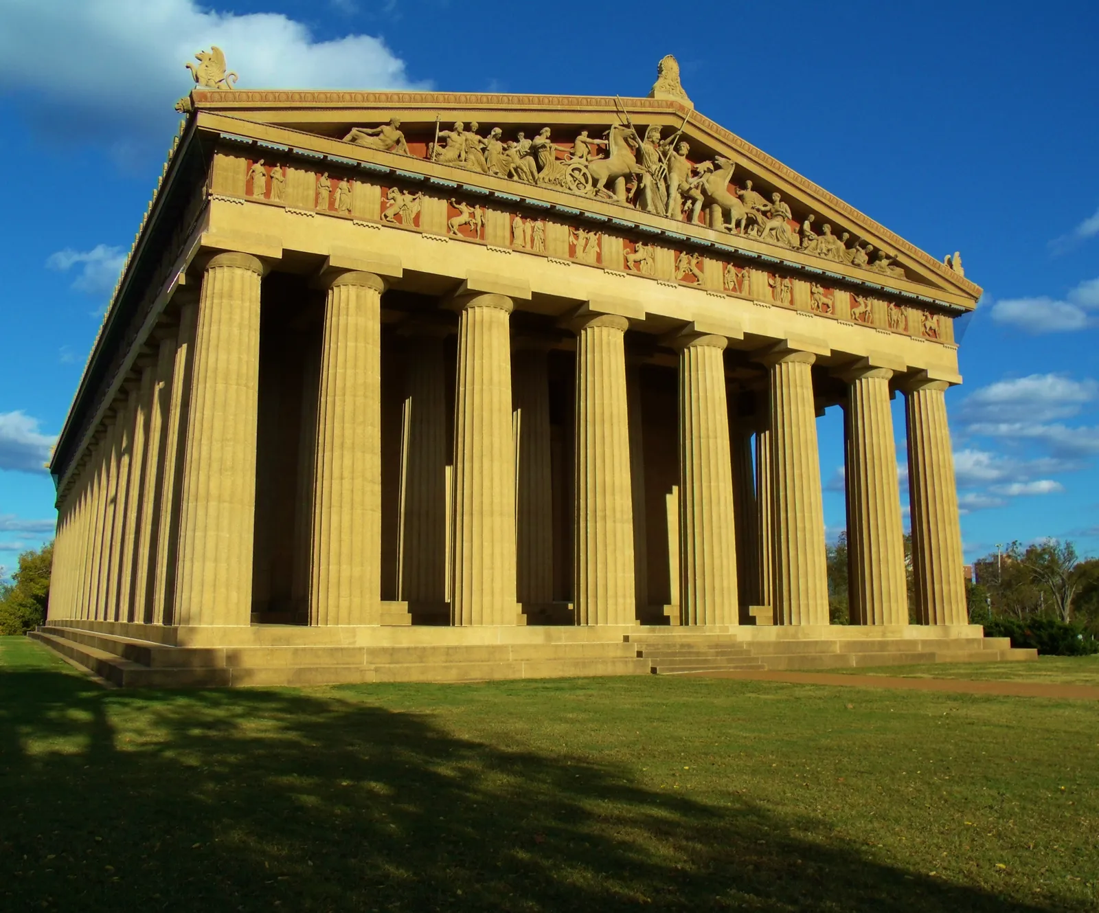 The Nashville Parthenon in low evening sun, its full Doric colonnade and carved pediment figures picked out in gold light against a dark blue sky