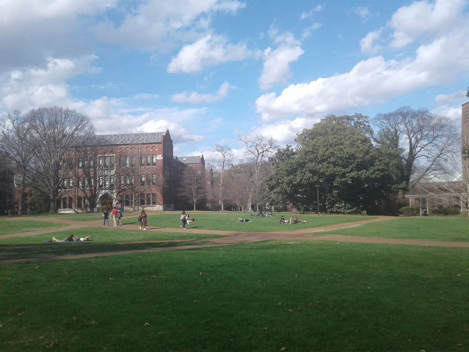 An open lawn on the Vanderbilt University campus in Nashville with students sitting on the grass and a red brick academic building among mature trees behind
