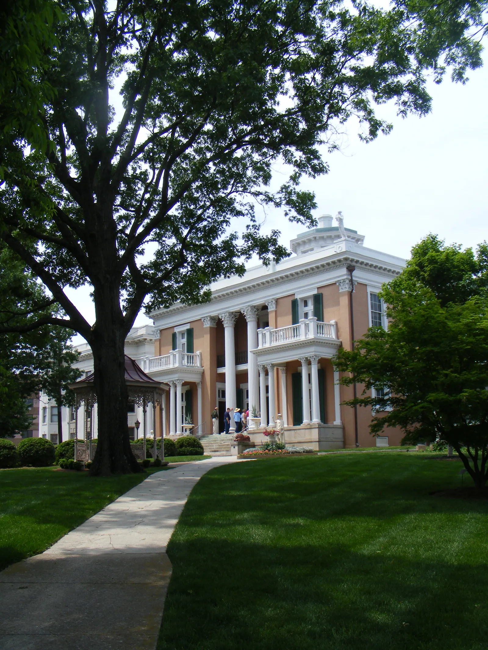 Belmont Mansion in Nashville, a pink Italianate villa with white columned porches, green shutters and a rooftop cupola, seen across a lawn under mature trees
