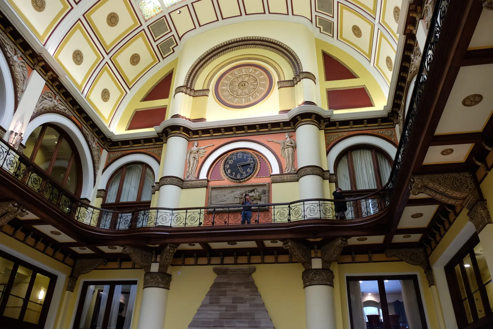 The lobby of Nashville's Union Station from below, with a coffered and stained-glass barrel ceiling, a balustraded gallery running around it and a large round clock relief on the far wall