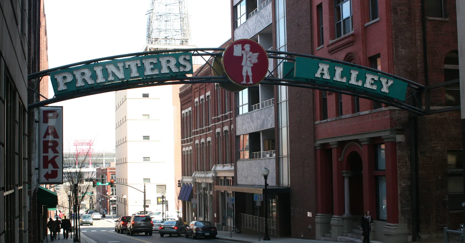 The green painted arch reading Printers Alley spanning the entrance to the alley in downtown Nashville, with brick buildings on both sides of the street
