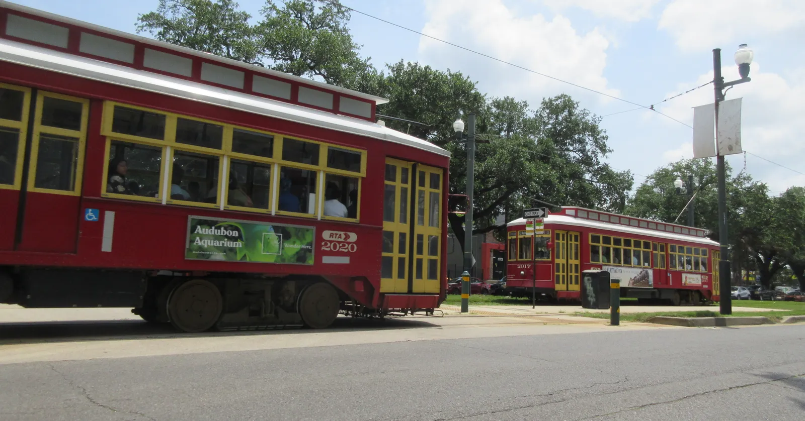 Two red streetcars passing on the grassed neutral ground down the middle of Canal Street in New Orleans, with palms and oaks on either side