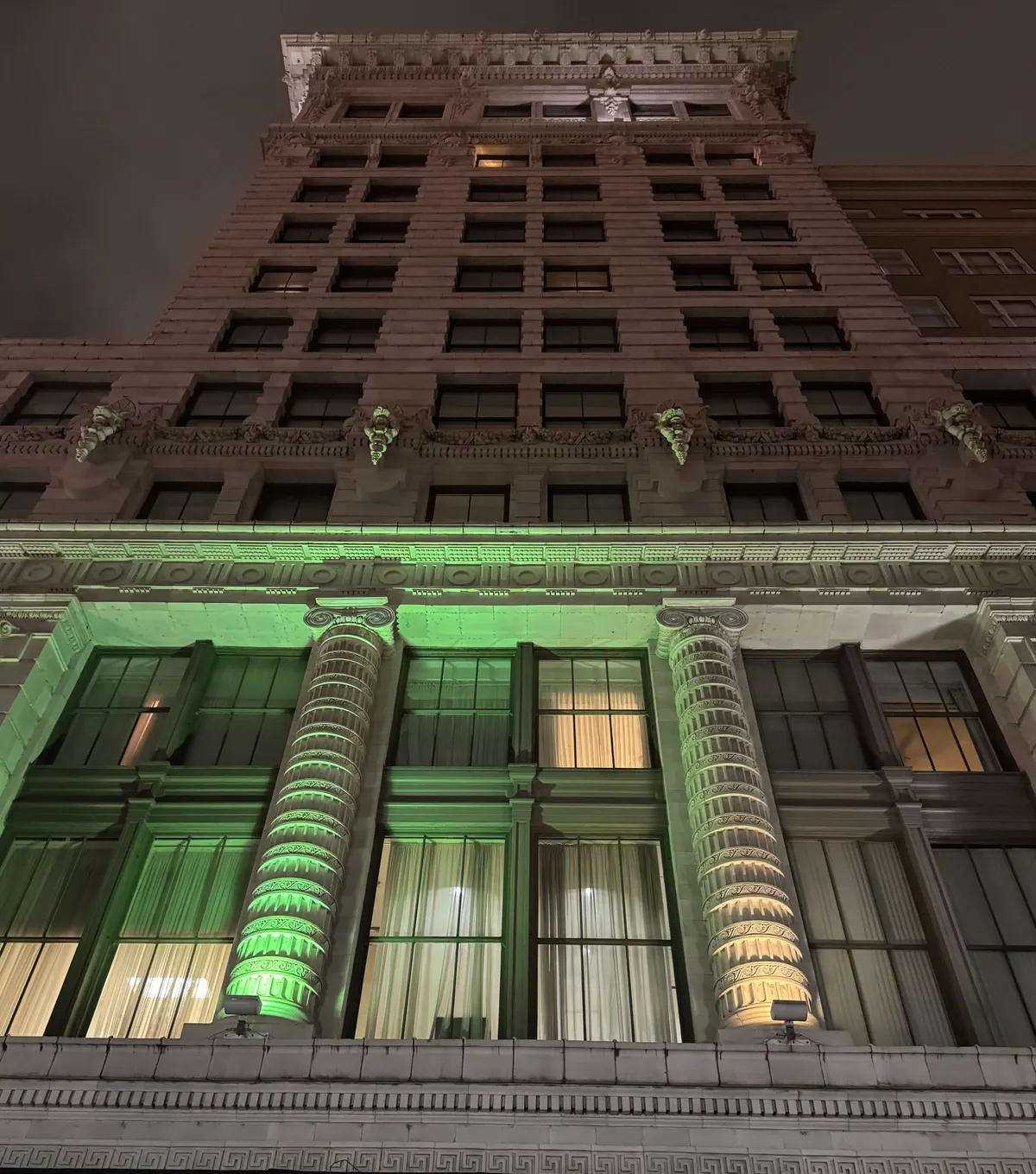 The Maison Blanche building on Canal Street in New Orleans lit from below at night, a tall pale terracotta facade with carved lion heads along a cornice and fluted columns at second-floor level