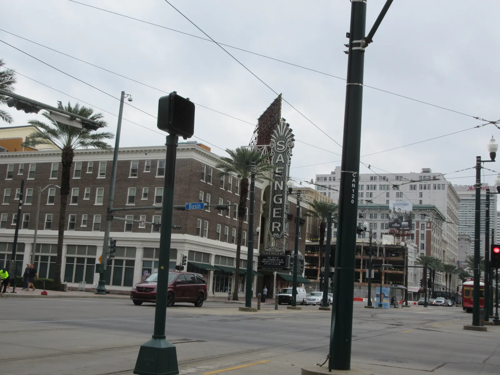 The tall vertical Saenger sign standing out over Canal Street in New Orleans, with the theatre's brick frontage below it and streetcar wires crossing overhead