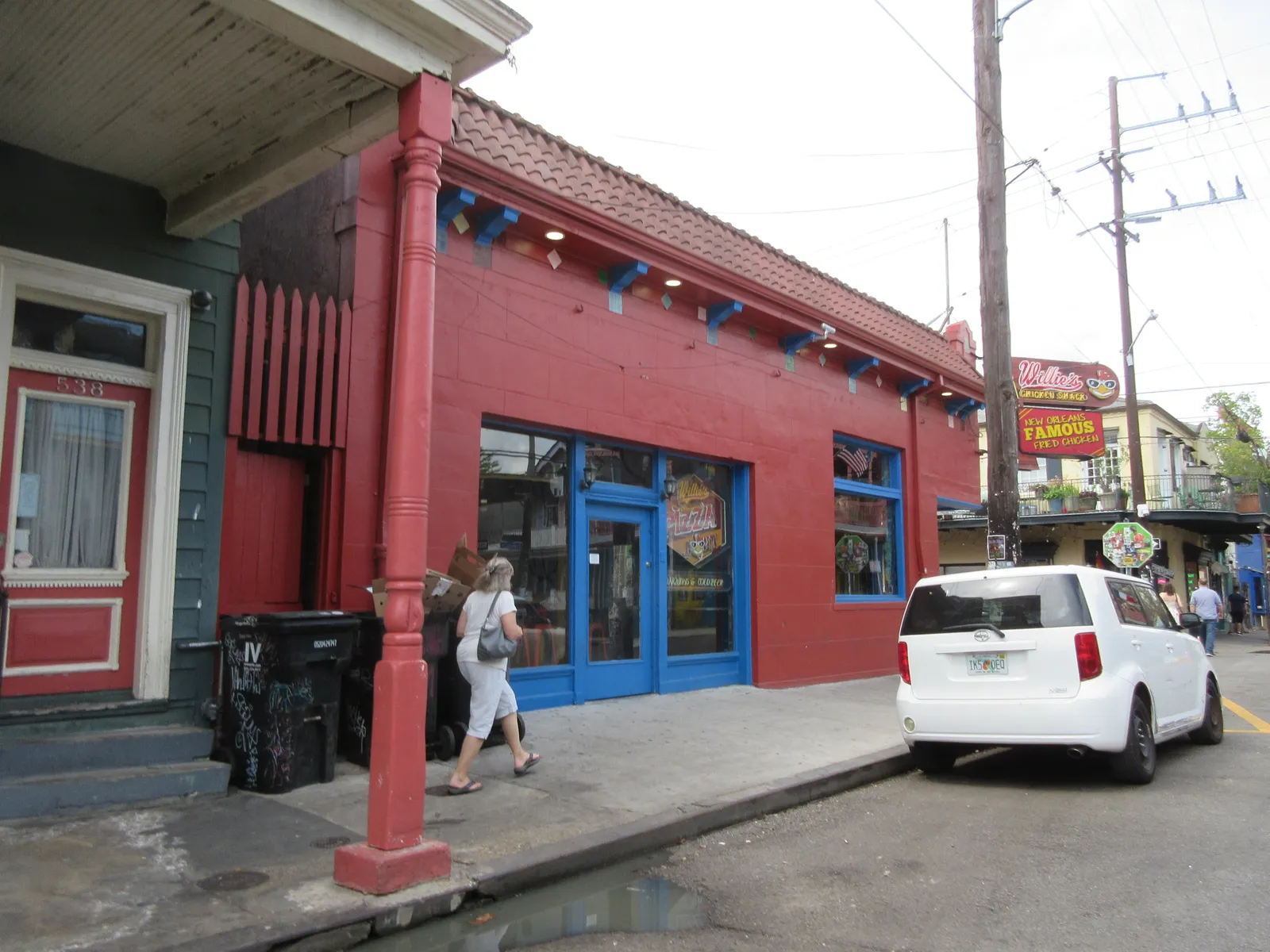 A dark red painted club frontage with blue window frames on Frenchmen Street in the New Orleans Marigny, an iron column at the corner and people walking past on the pavement