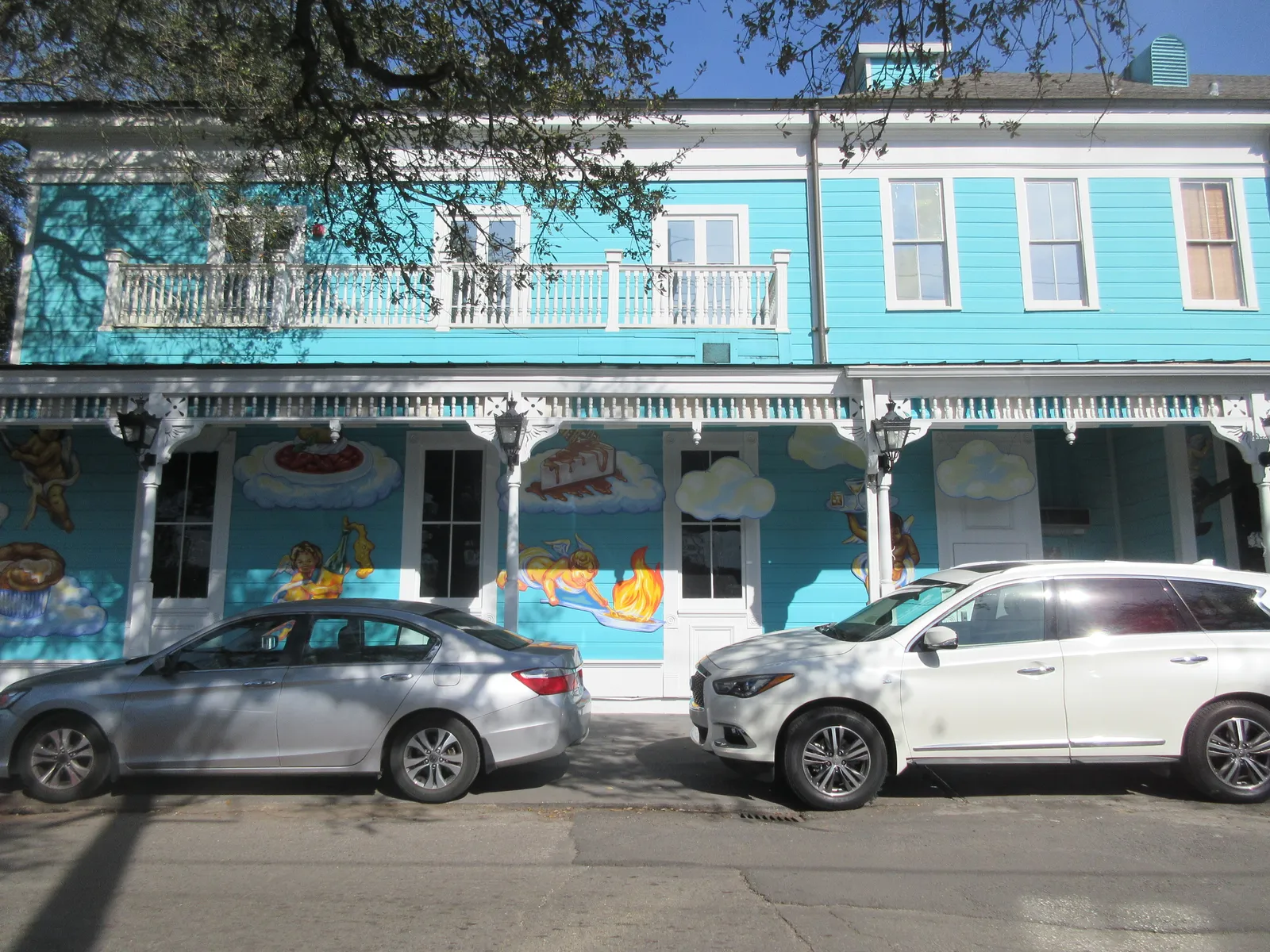 The turquoise and white painted exterior of Commander's Palace restaurant on Washington Avenue in New Orleans, with white balcony railings above and awnings over the ground-floor windows