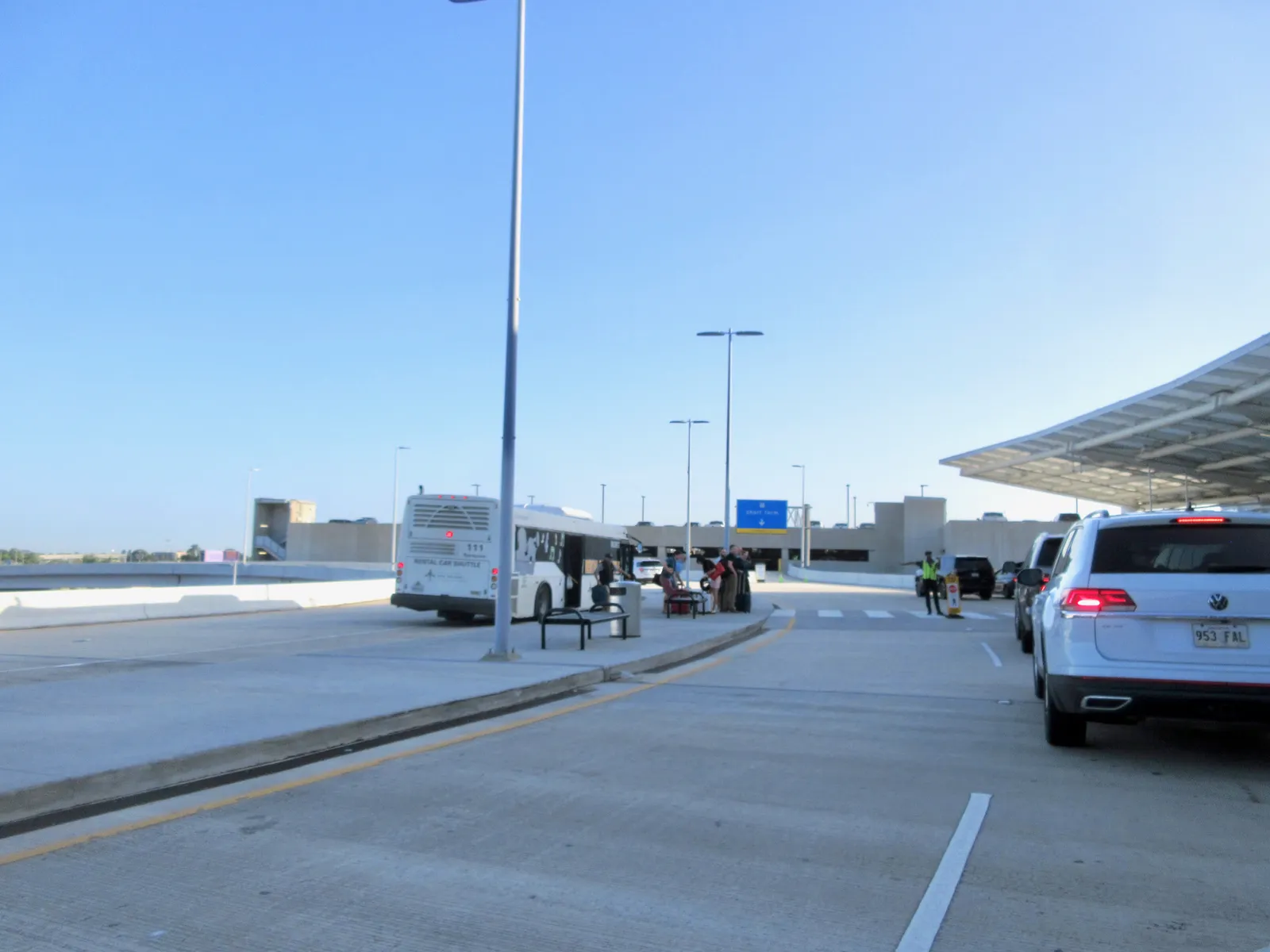 The departures roadway at the New Orleans airport terminal, a shuttle bus pulled up at the kerb under the edge of the terminal's white canopy