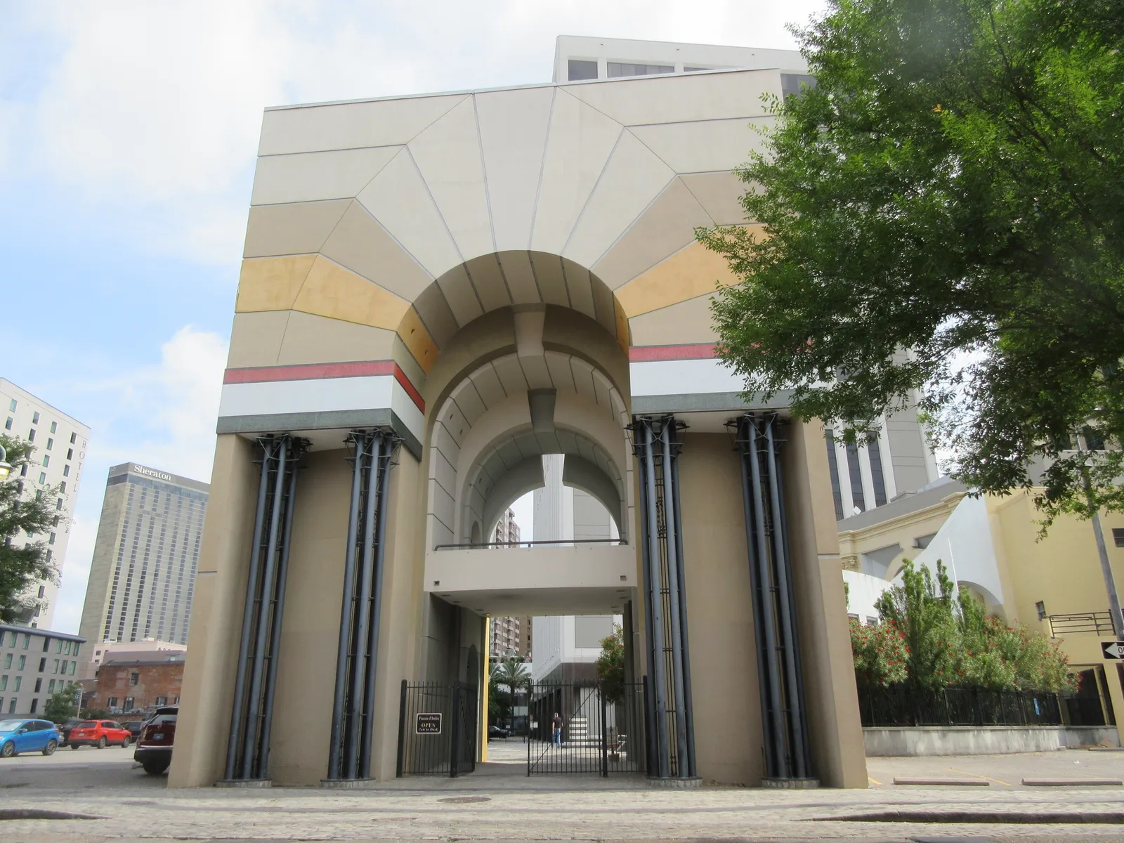 The entrance arch of the Piazza d'Italia in New Orleans seen from Commerce Street, a tall postmodern gateway in tan and grey stepped stone with dark slender columns and a band of red and yellow across the top