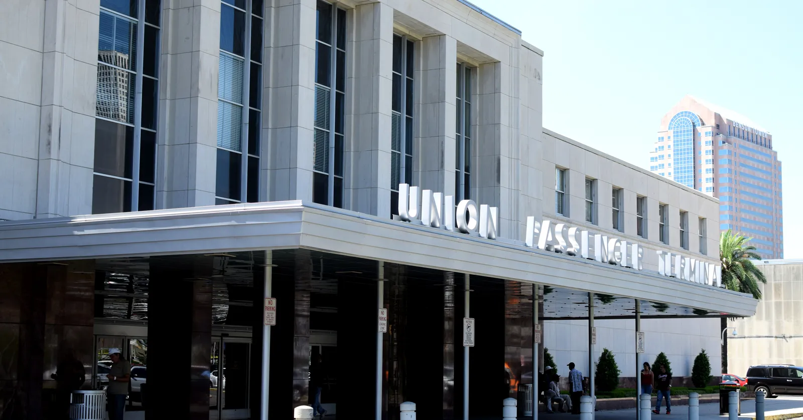 The front of New Orleans Union Passenger Terminal on Loyola Avenue, a low grey modernist building with tall pilasters and the words Union Passenger Terminal in aluminium letters along the canopy
