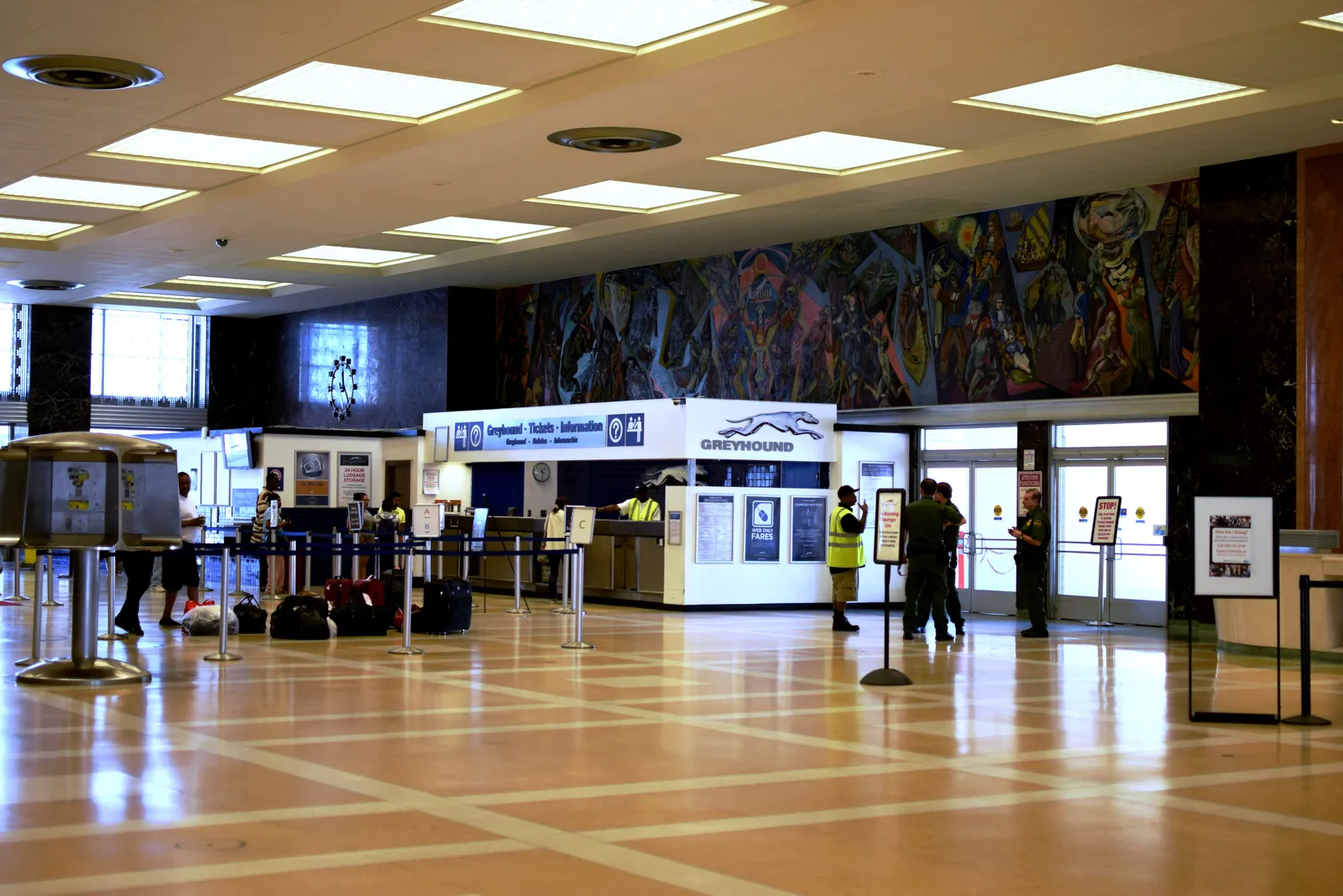 The waiting hall inside New Orleans Union Passenger Terminal, a wide polished floor with a ticket counter across the far end and a long painted mural panel running along the wall above it