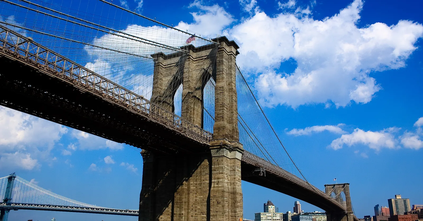 One of the Brooklyn Bridge's granite towers with its two gothic arches, cables fanning out either side and the Manhattan Bridge visible further up the East River