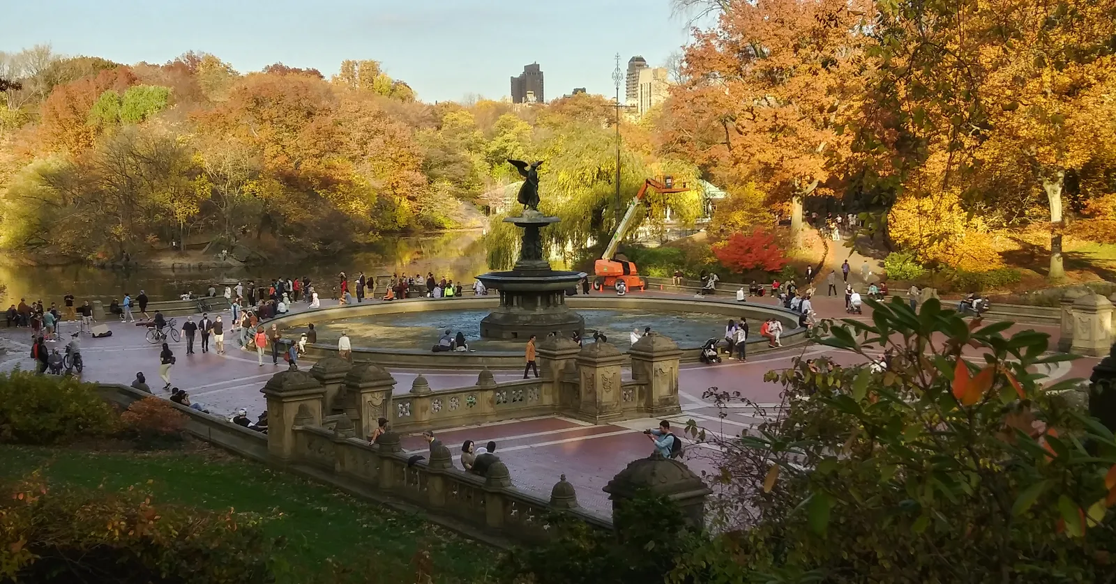 Bethesda Terrace in Central Park in autumn, the winged Angel of the Waters standing over the fountain basin with people around the paved terrace and orange trees behind