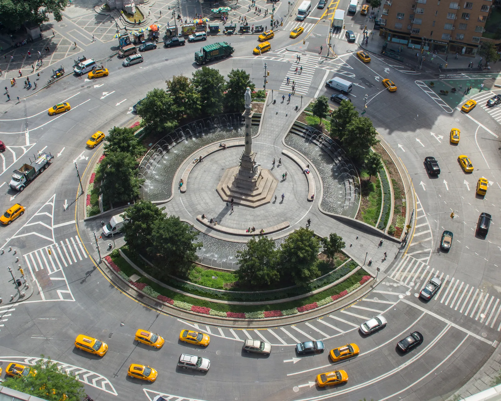Columbus Circle seen from above, a planted traffic circle with a tall column at its centre and yellow taxis running round the outside of it