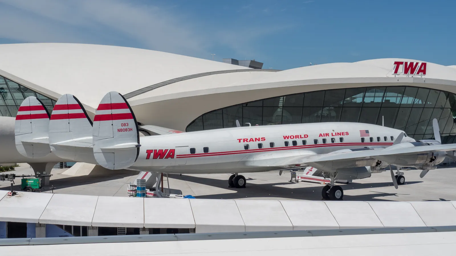 A restored red and white Lockheed Constellation airliner in Trans World Airlines livery parked on the apron in front of the TWA Flight Center's curved white roof