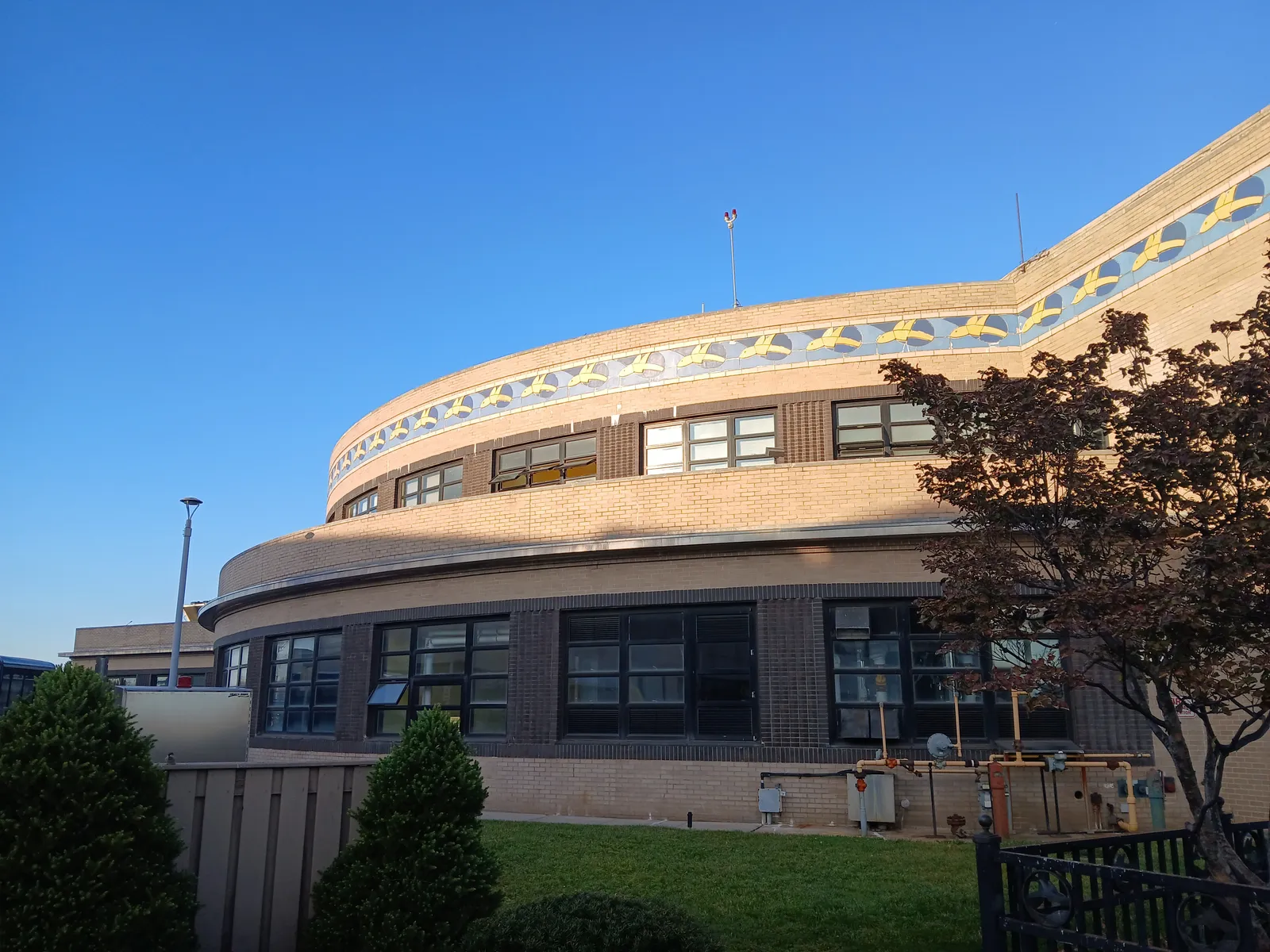 The curved brick rotunda of the Marine Air Terminal at LaGuardia Airport, a frieze of stylised yellow flying fish running around it below the roofline against a blue sky