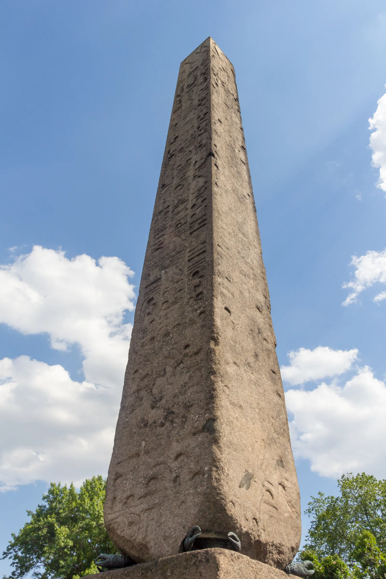 Cleopatra's Needle in Central Park, a weathered granite obelisk covered in hieroglyphs rising against a blue sky with trees at its base