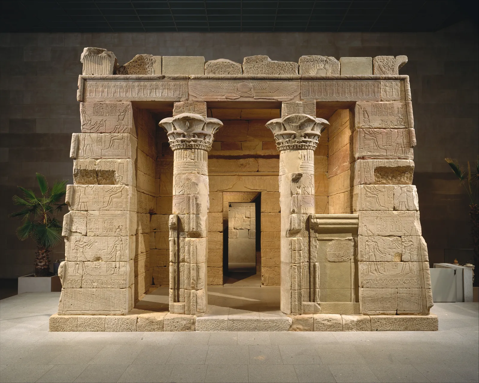 The Temple of Dendur reassembled inside the Metropolitan Museum of Art, a sandstone gateway and temple front with carved columns standing on a stone platform in a bare hall