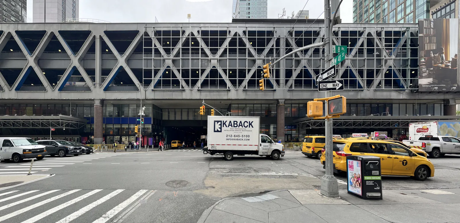 The Port Authority Bus Terminal on Eighth Avenue, a long concrete deck on cross-braced steel supports carrying bus ramps over the street, with taxis waiting at the crossing