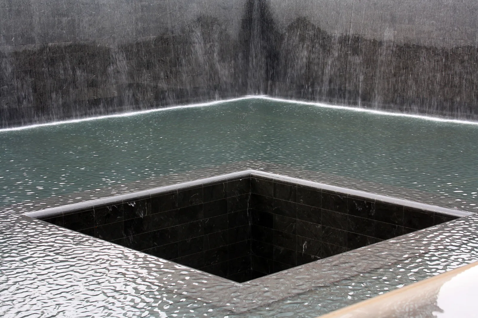 One of the 9/11 Memorial pools, water falling down all four granite walls into a square basin and disappearing into a second smaller void at its centre