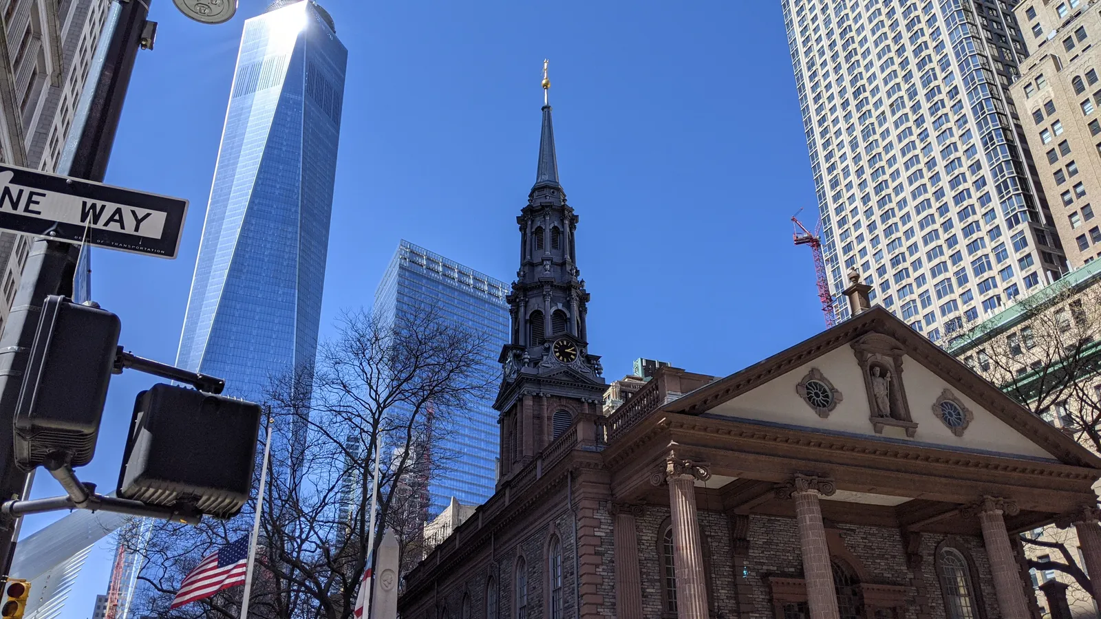 St Paul's Chapel on Broadway, a Georgian stone church with a columned portico and a slender spire, One World Trade Center rising behind it against a blue sky