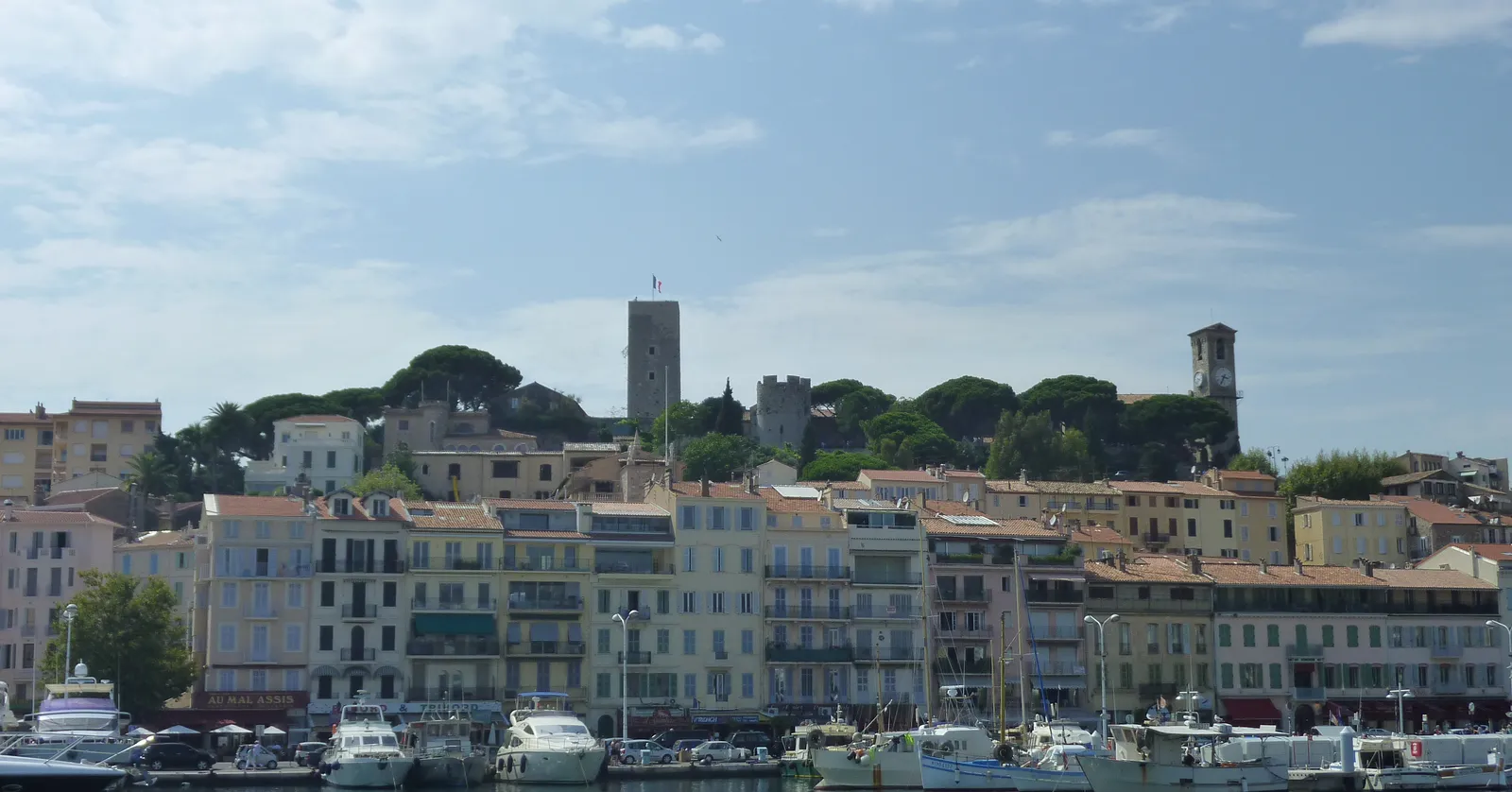 The old Suquet quarter of Cannes rising above the harbour, a hill of pale houses topped by a medieval watchtower and a church tower among pine trees, with yachts moored below