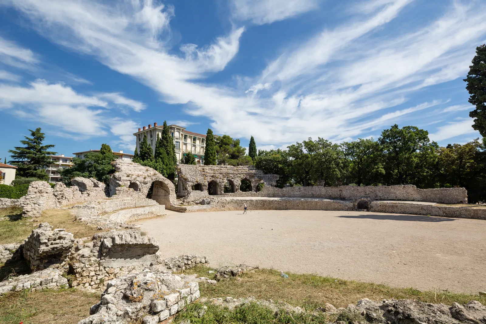 The ruins of the Roman amphitheater at Cimiez in Nice, with arched stonework and trees under a blue sky