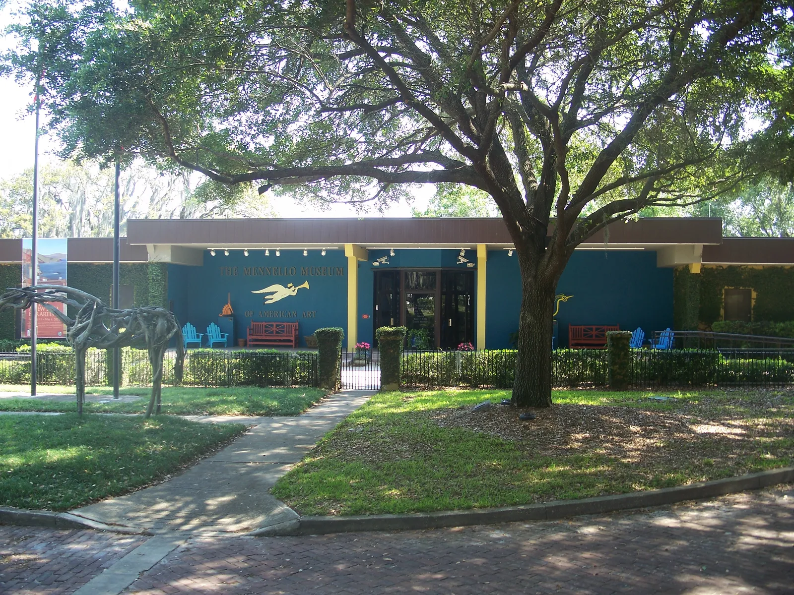 The low teal-painted building of the Mennello Museum of American Art in Orlando, shaded by a spreading oak with a lawn and railings in front of it