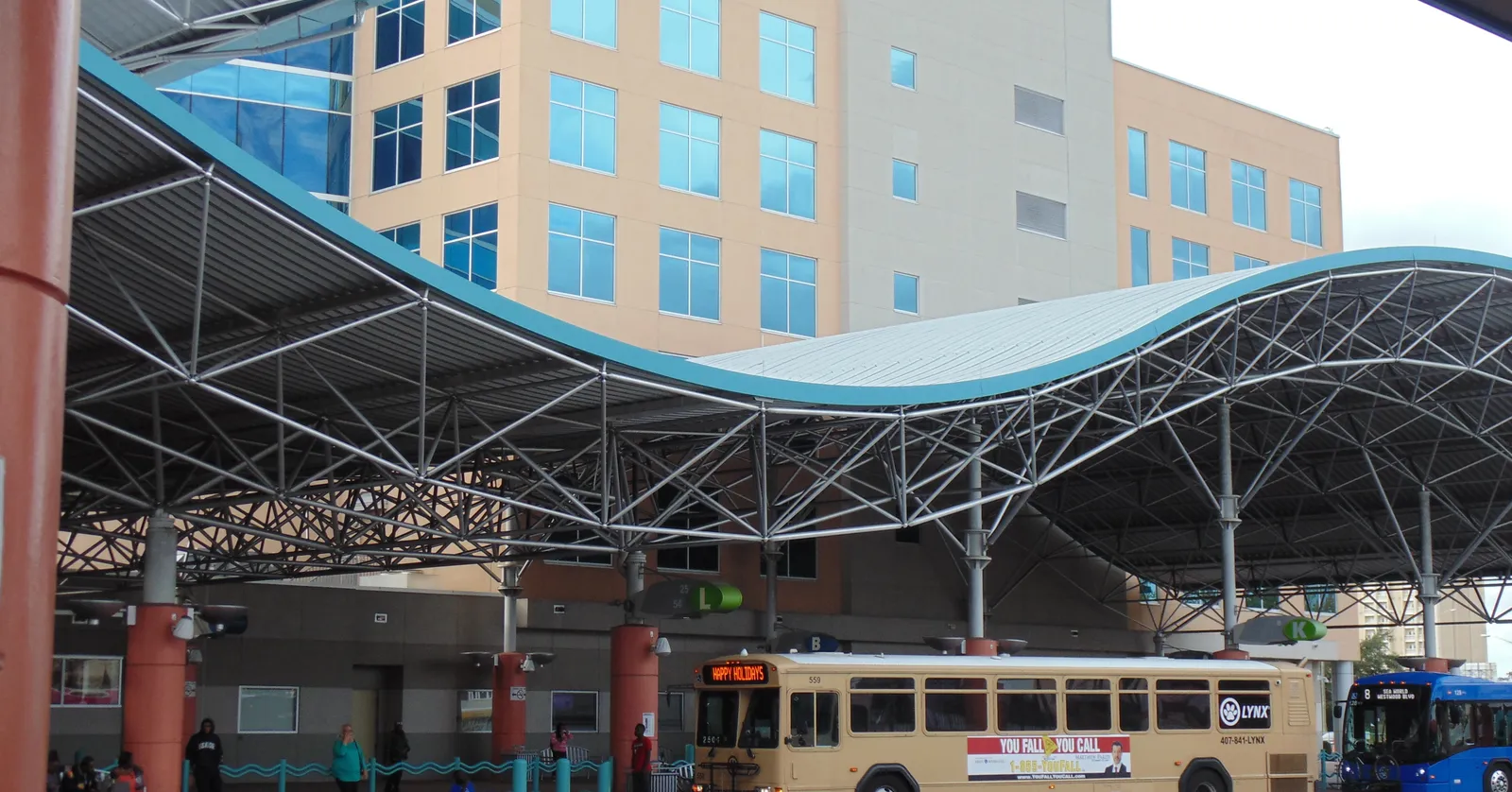 Buses parked under the curved steel canopy of Lynx Central Station in Orlando, with the station's office block rising behind it