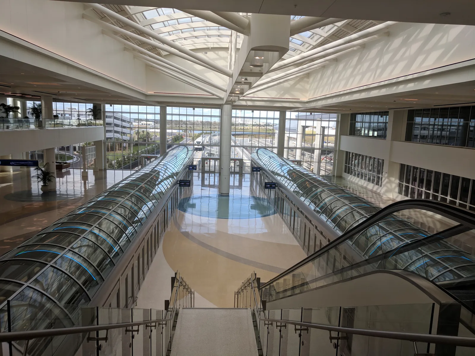 The skylit hall of Orlando International Airport's Intermodal Terminal, with two glass-tubed moving walkways running away beneath a white steel roof