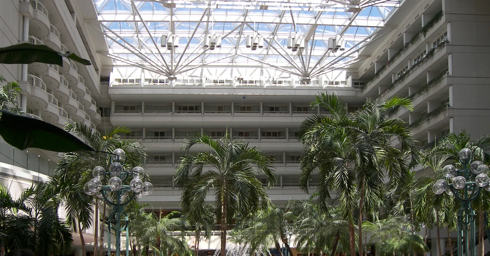 The main terminal atrium at Orlando International Airport, full-size palm trees and a fountain under a steel-and-glass roof with hotel balconies overlooking it