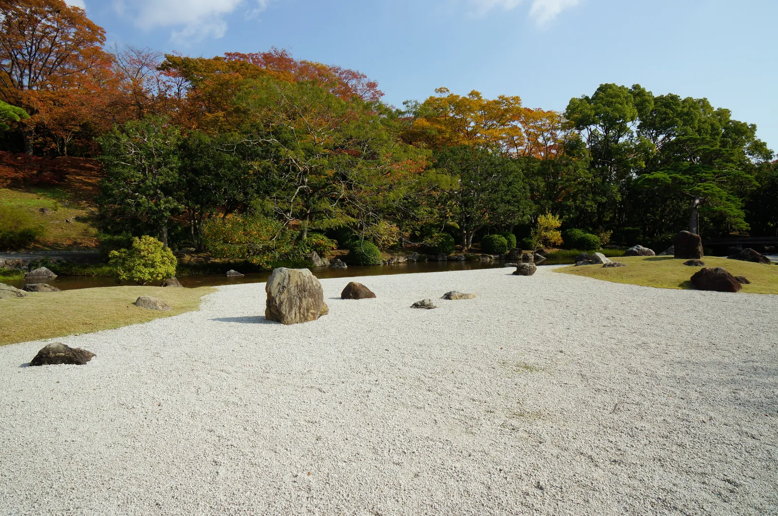 A dry garden in Expo '70 Commemorative Park, a wide bed of raked white gravel set with low dark boulders, backed by a line of trees turning red and gold in autumn