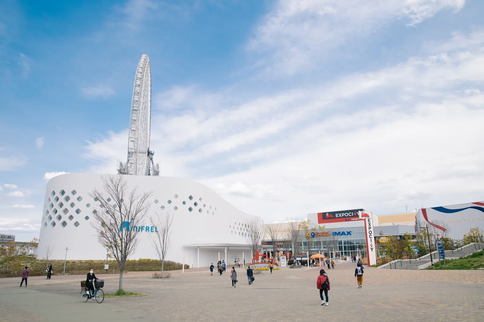 The NIFREL building at Expocity in Suita, a low white drum punched with round windows, with the white lattice of a tall Ferris wheel rising directly behind it and the Expocity shopping complex to the right