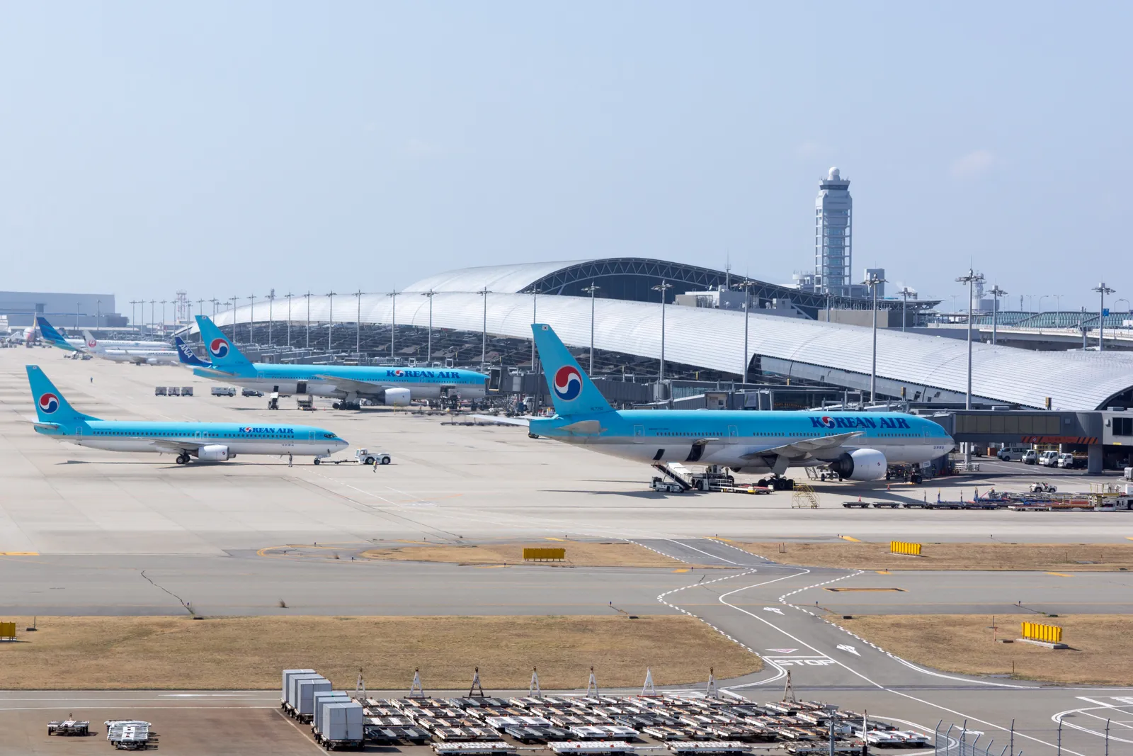 Jets parked at the curved Terminal 1 building of Kansai International Airport, seen across the apron from the Sky View observation hall, with the control tower behind