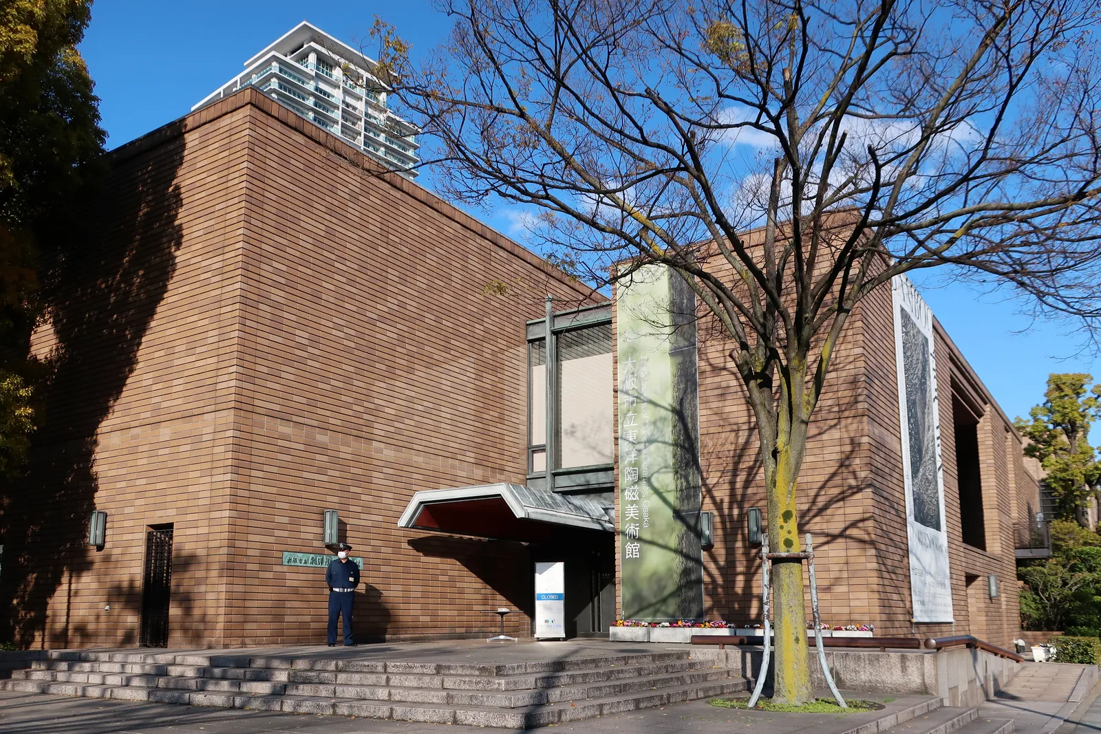 The Museum of Oriental Ceramics in Osaka, a low brown brick block with a recessed glazed entrance bay, approached up a short flight of steps between bare trees