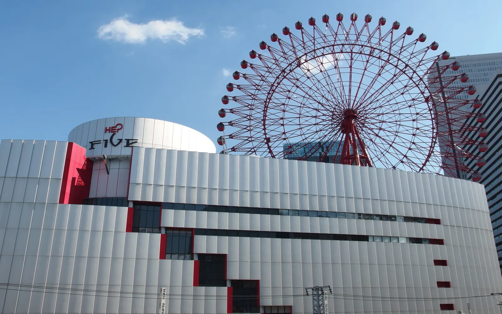 The HEP FIVE building in Umeda, a white ribbed shopping block with a red whale logo, and a large bright red Ferris wheel rising directly out of its roof against a blue sky