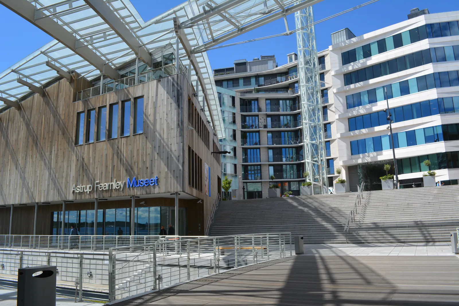 The entrance front of the Astrup Fearnley Museum on Tjuvholmen, a low timber-clad building with the museum's name lettered across it, under a curved glass canopy carried on slim steel masts