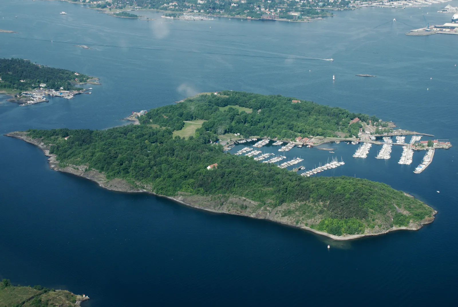 Hovedøya from the air, a low wooded island in the Oslofjord with open meadows in its centre and a marina full of small boats along one shore