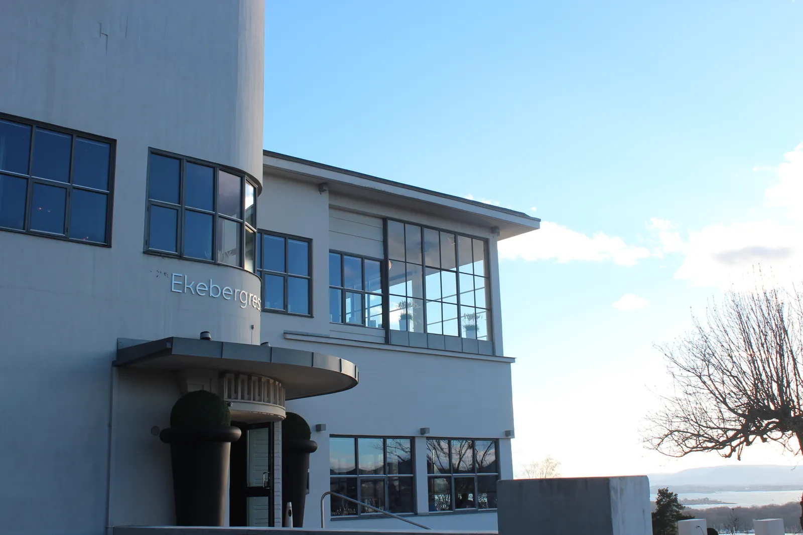 Ekebergrestauranten in Oslo, a white functionalist building with a curved corner, ribbon windows and a flat canopy over the entrance, standing against a clear sky