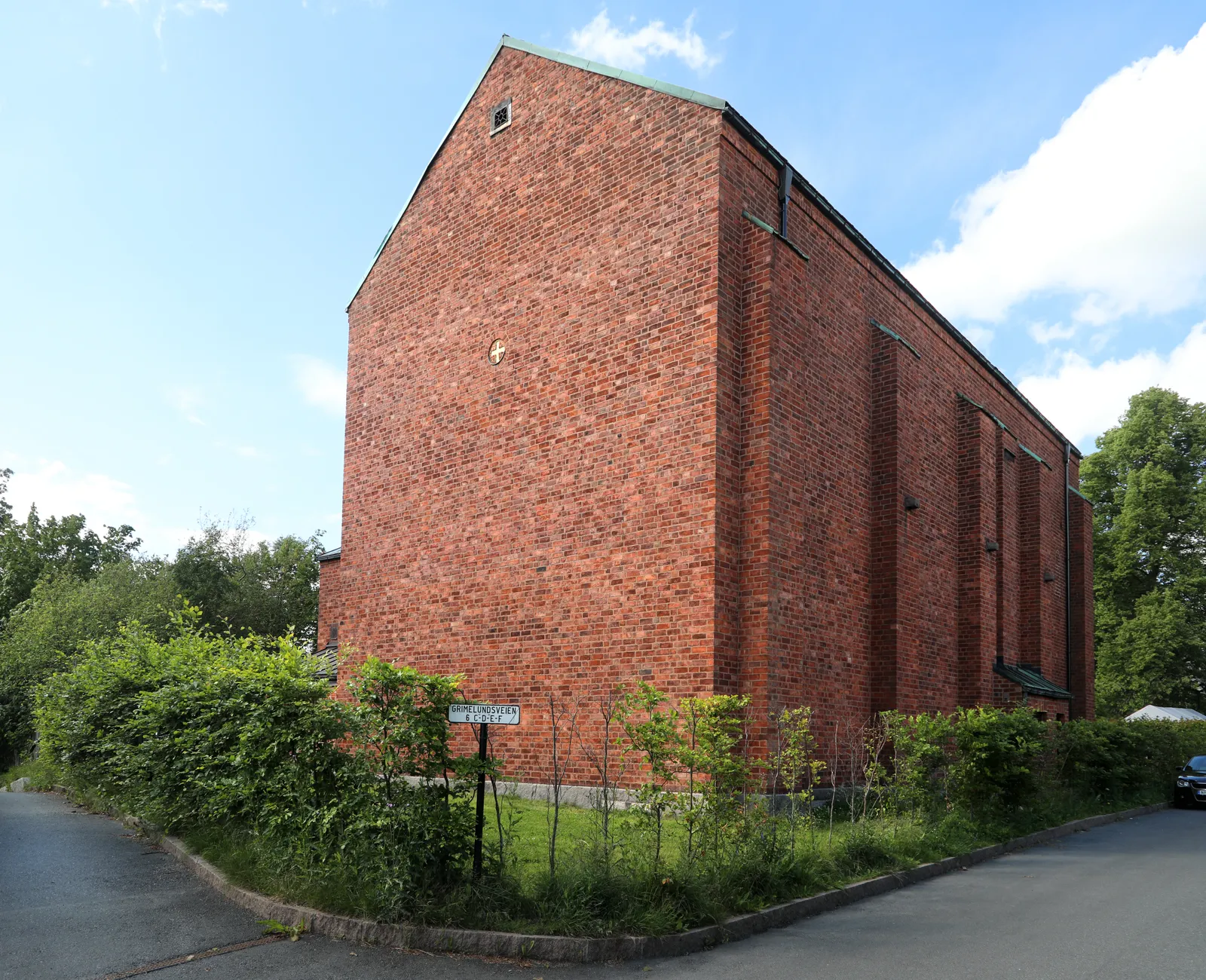 The Emanuel Vigeland Museum at Slemdal in Oslo, a plain red brick block with no windows in its end wall, standing behind a hedge on a quiet residential street