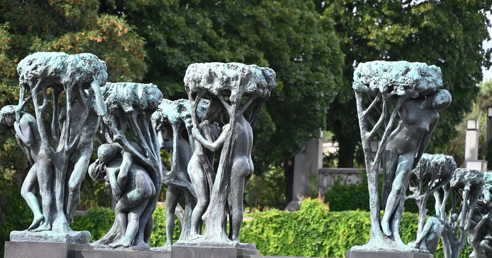 Bronze figure groups on granite plinths around the fountain in Frogner Park, Oslo, each group a cluster of human figures holding up the spreading canopy of a bronze tree