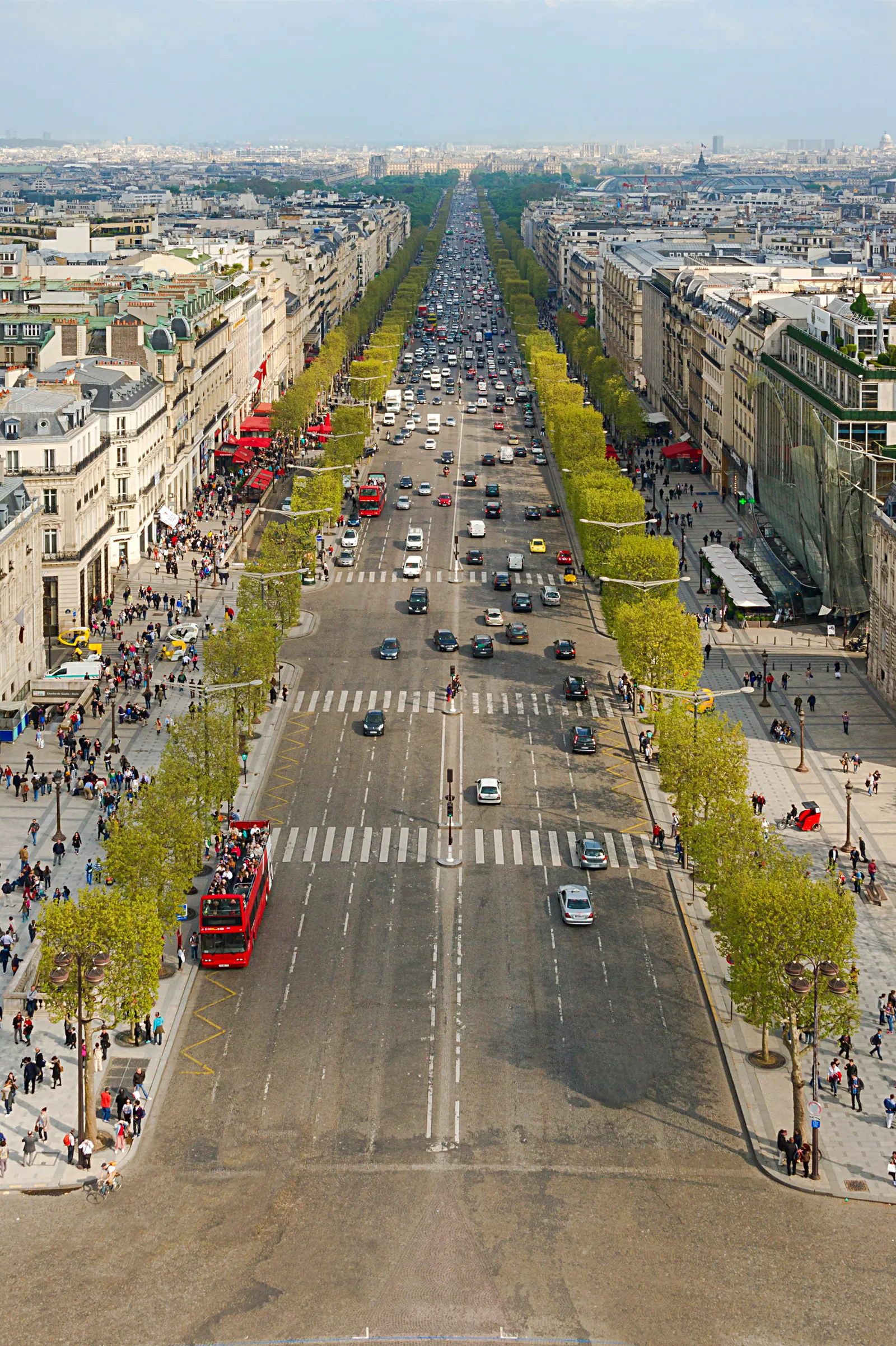 Looking down the Champs-Élysées from the roof of the Arc de Triomphe in Paris, the avenue running dead straight between two lines of clipped trees with traffic filling all eight lanes