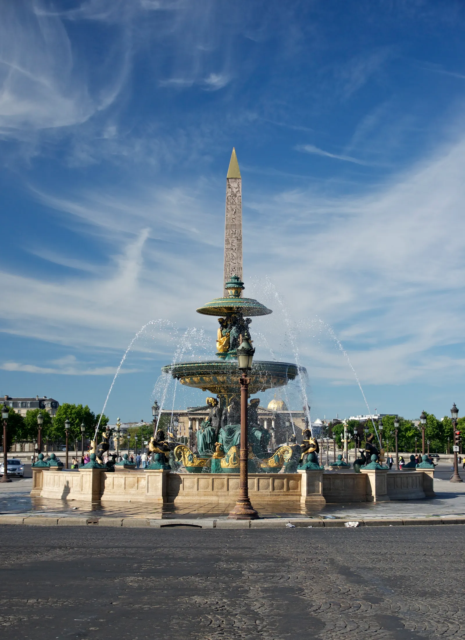 One of the bronze fountains on the Place de la Concorde in Paris playing in the sun, with the Luxor obelisk and its gilded cap standing directly behind it