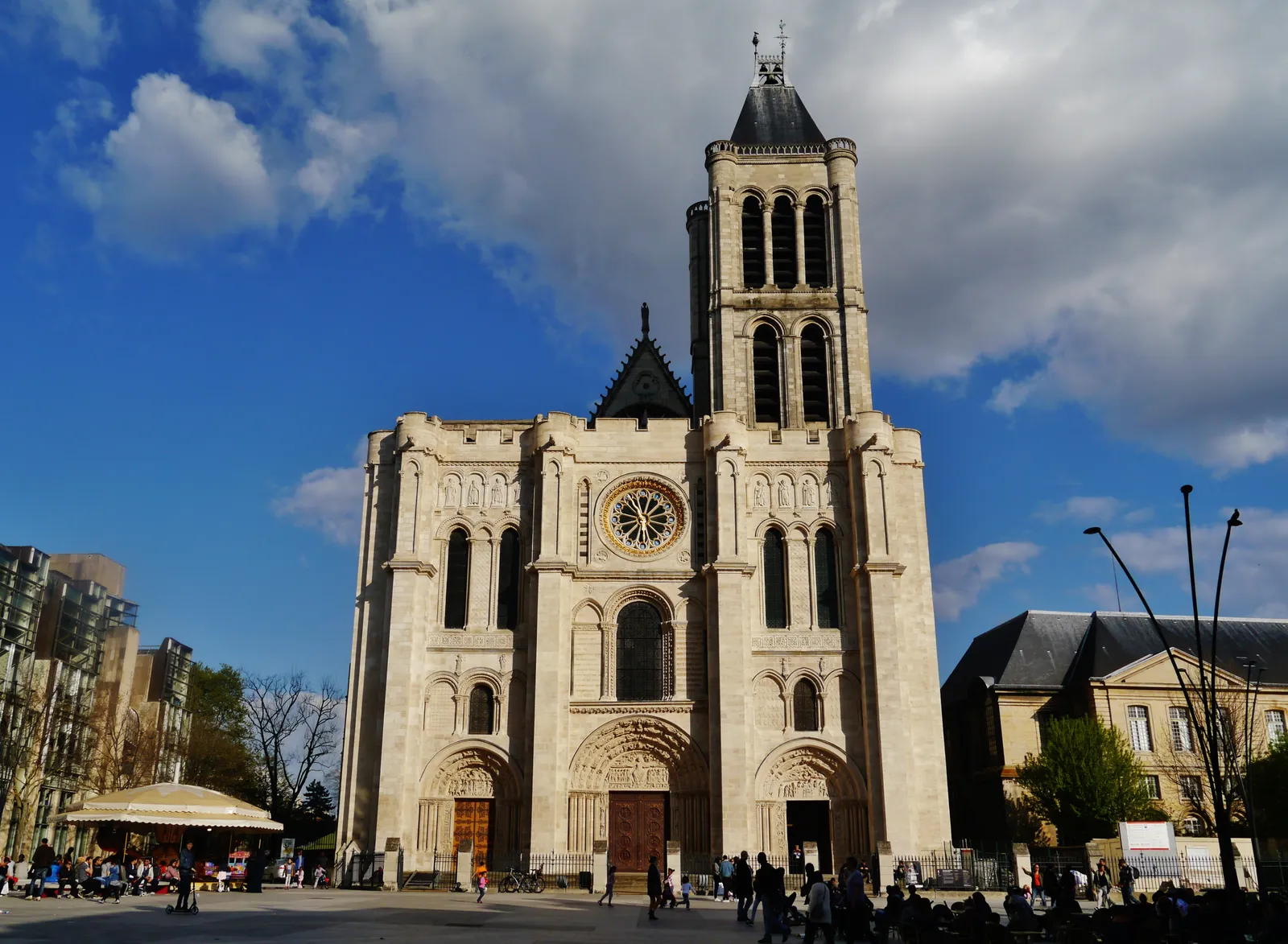 The pale stone west front of the Basilica of Saint-Denis north of Paris, with its rose window, three portals and a single square tower against a blue sky