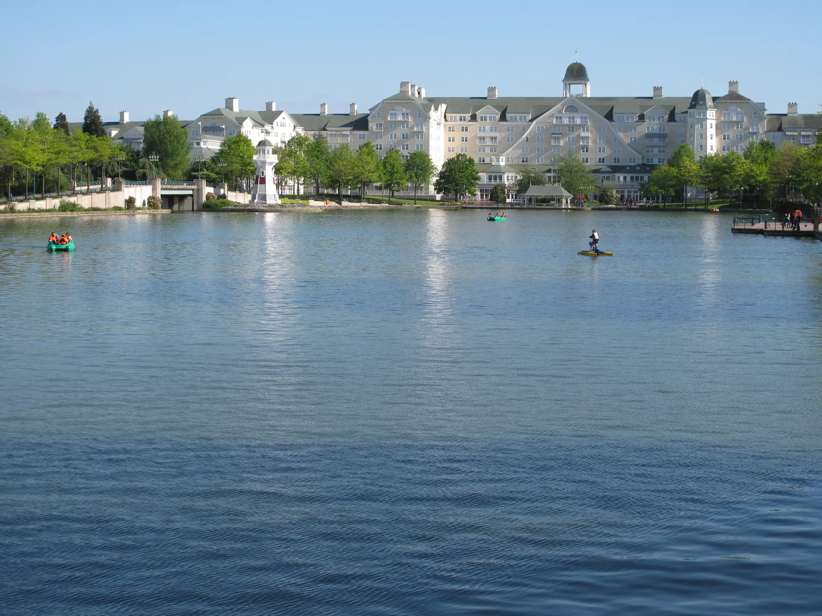 Lake Disney with pedal boats on the water and a lakeside hotel with a small lighthouse in the background